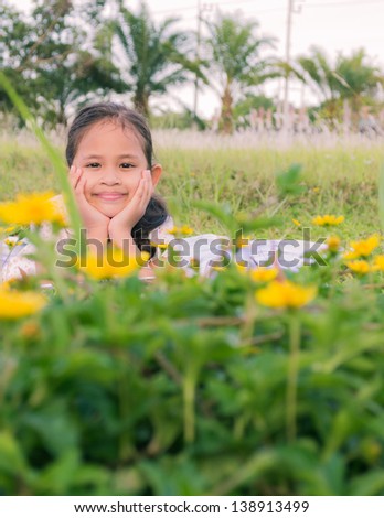 A cute girl lie down on a field behind yellow flowers