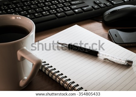 Pen on notebook with computer keyboard, mouse and cell phone on wooden table