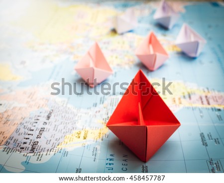 Paper boats following a red leader boat on world map. Concept for leadership, teamwork and winning success