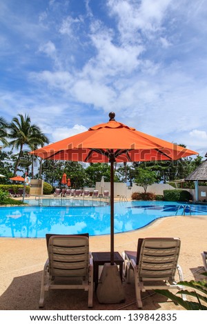 Orange umbrella at the open swimming pool and sky background