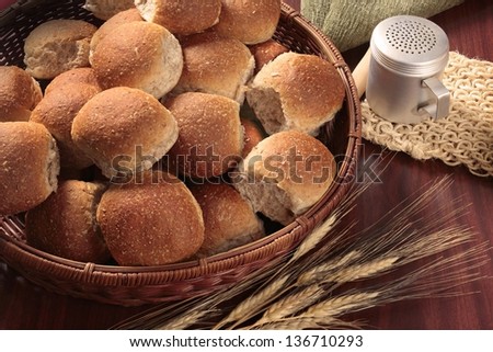 Freshly baked whole wheat buns in basket on wooden table, wheat in front