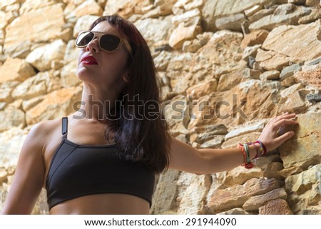 Beautiful young model on wooden sunglasses and sports outfit looking at the sun, inside an abandoned house.