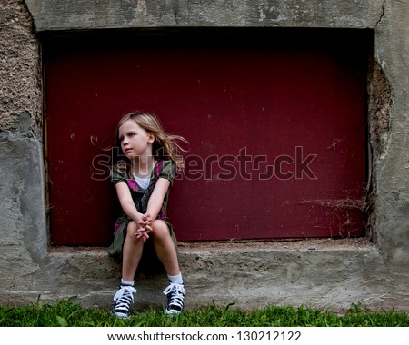 Serious little girl on concrete ledge with blowing hair