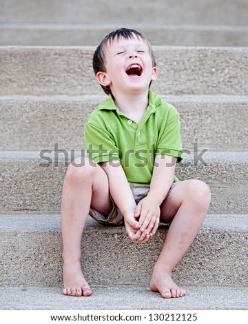Little boy sitting on concrete steps laughing with joy