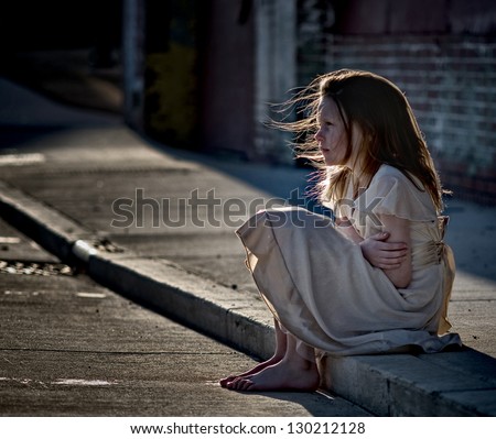 Little girl sitting on curb in dirty dress looking cold and alone