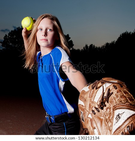 Girl in blue jersey at night leading with mitt and throwing softball