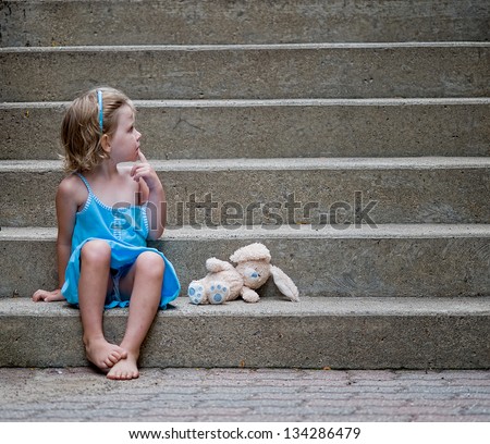 cute little girl wearing blue dress sitting on concrete steps with her stuffed bunny