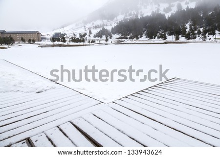 snowed dock over a frozen lake with mountains and a hotel at the back  /Winter landscape Pyrenees./ \