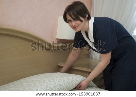 Maid making bed in hotel room
