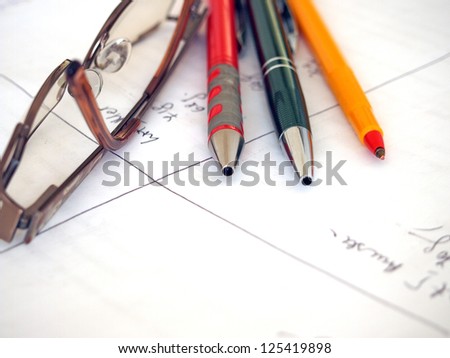 Glasses and writing instruments on a hand written paper