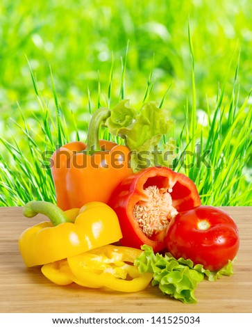 Bell pepper and tomato on a bamboo board on the green grass background