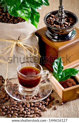 Coffee cup with saucer, coffee mill, bag with coffee tree and beans on the sackcloth