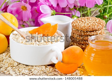 Oatmeal with apricot in the bowl, milk jug, cookies, honey and flowers