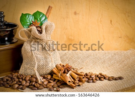 Coffee grains with cinnamon and anise on sackcloth with bag, leaves and coffee mill