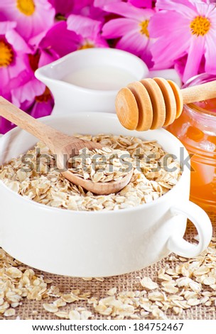 Oatmeal in the bowl, honey, milk jug and flowers