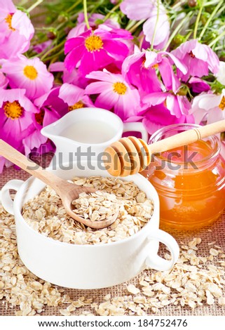Oatmeal in the bowl, honey, milk jug and flowers