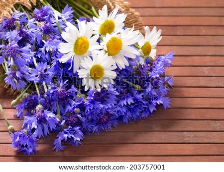 Field bouquet of daisies and cornflowers on the wooden board