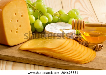 Round camembert cheese, smoked cheese, honey, walnuts and grapes on the wooden board