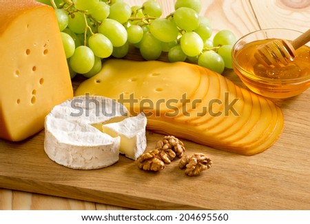 Round camembert cheese, smoked cheese, honey, walnuts and grapes on the wooden board