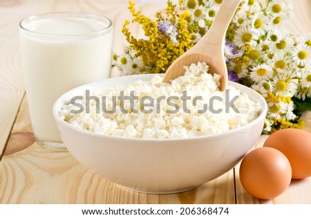 Cottage cheese in bowl with wooden spoon,  milk and eggs on the meadow flowers background