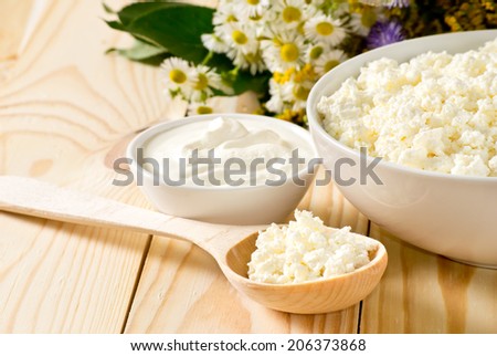 Cottage cheese in bowl with wooden spoon and sour cream on the meadow flowers background