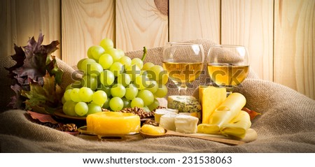 White wine with blue cheese, camembert and swiss cheese, walnuts, honey and grapes on sackcloth on a background of a wooden wall and autumn leaves