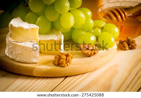 Round camembert cheese, smoked cheese, honey, walnuts and grapes on the wooden board. For this photo applied vignetting effect.