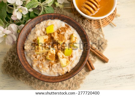 Oatmeal with apple, honey and cinnamon in the bowl and cinnamon sticks on the wooden board