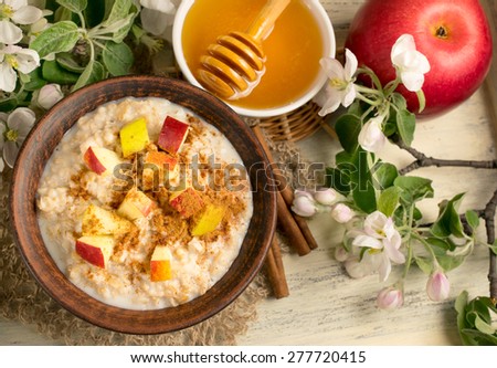 Oatmeal with apple, honey and cinnamon in the bowl and cinnamon sticks on the wooden board
