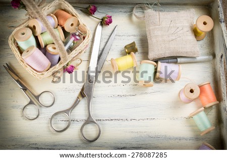 Different colored spools of thread, scissors, needle and thimble for sewing on wooden boards in the  Shabby Chic style. For this photo applied vignetting effect.