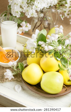 Yellow apples on the plate with twig of apple tree, milk, honey and knitted napkin on the wooden tray in Shabby Chic style