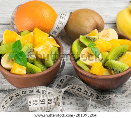 Fruit salad with kiwi, banana and orange for slimming and centimeter on the wooden board