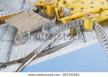 Set of reel of thread, scissors, centimeter, toothed wheel, thimble, fabric, needle and pins for sewing and needlework in Shabby Chic style. Still life photo with tools for handmade.