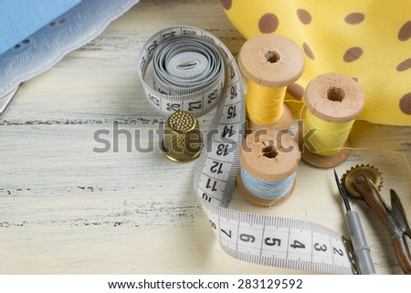 Set of reel of thread, centimeter, fabric, thimble, seam ripper and toothed wheel for sewing and needlework on the wooden board in Shabby Chic style. Still life photo with tools for handmade.