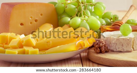 Round camembert cheese with smoked cheese, walnuts, honey and grapes on the wooden board