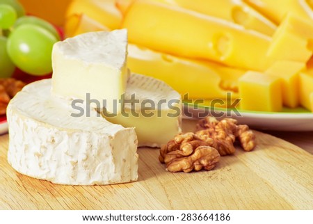 Round camembert cheese with smoked cheese, walnuts and grapes on the wooden board