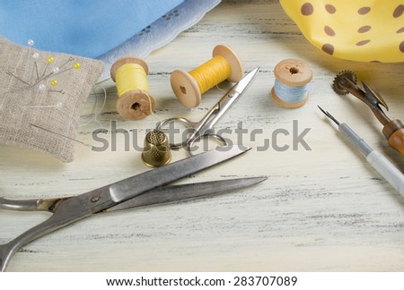 Set of reel of thread, centimeter, fabric, thimble and scissors, seam ripper, toothed wheel, needle and pins for sewing and needlework on the wooden board in Shabby Chic style.