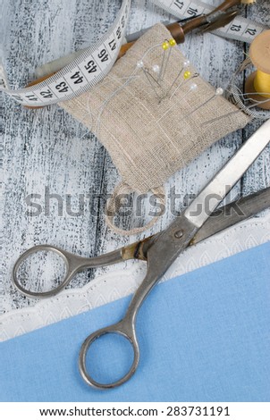 Set of reel of thread, centimeter, fabric and scissors, toothed wheel, needle and pins for sewing and needlework on the wooden board in Shabby Chic style.