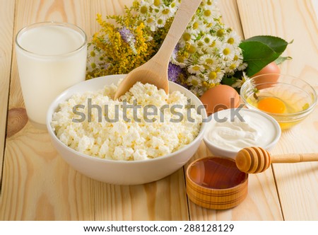 Cottage cheese in bowl with wooden spoon, milk, sour cream and eggs on the meadow flowers background