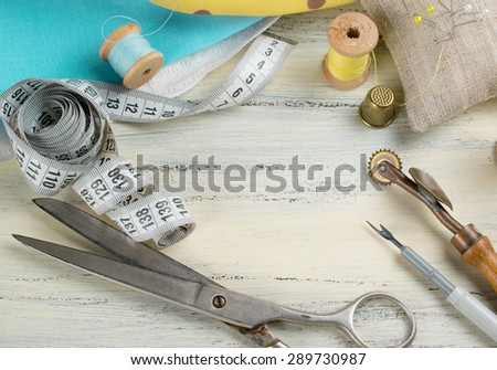 Set of reel of thread, centimeter, fabric, thimble and scissors, seam ripper, toothed wheel, needle and pins for sewing and needlework on the wooden board in Shabby Chic style.