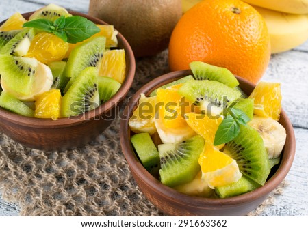 Fruit salad with kiwi, banana, orange and mint in the bowl, openwork napkin on the wooden board