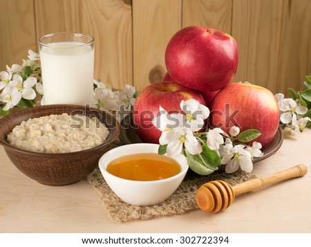 Red apples with oatmeal, milk and honey, twig of apple tree on the background of wooden wall.