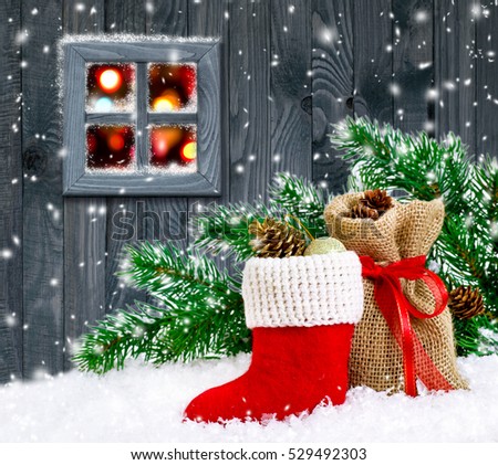 Santa\'s boot and bag with gifts and cones on wooden wall background and glowing lights outside the window
