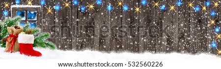 Christmas banner. Santa boot and bag with gifts and cones on wooden wall background and glowing lights outside the window.