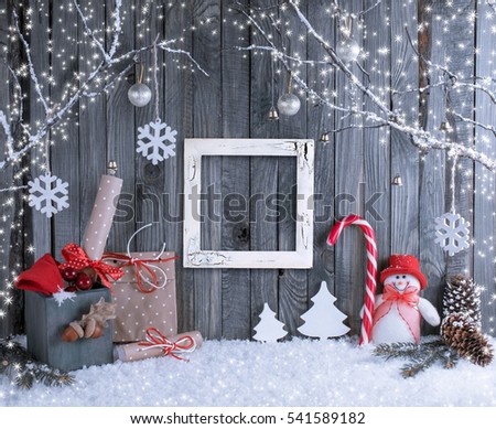 Christmas interior with snowman, photo frame, decorative branches, presents and candy canes on wooden planks background. New Year winter composition.