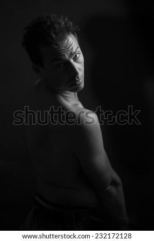 Black and white low key portrait of cute man with bare shoulder and black background