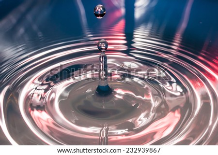 Water drop and concentric waves with column of water that rise again with blue and red light background