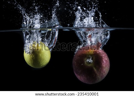Lemon and red apple falling into the water with big splash and air bubbles with black background