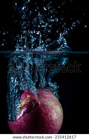 Red apple close up fall in water with blue air bubbles and swirl in a black background