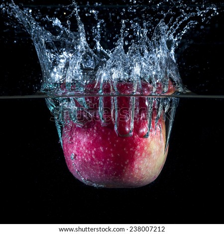 Isolated red apple fall in water with big blue splash and air bubbles in black background